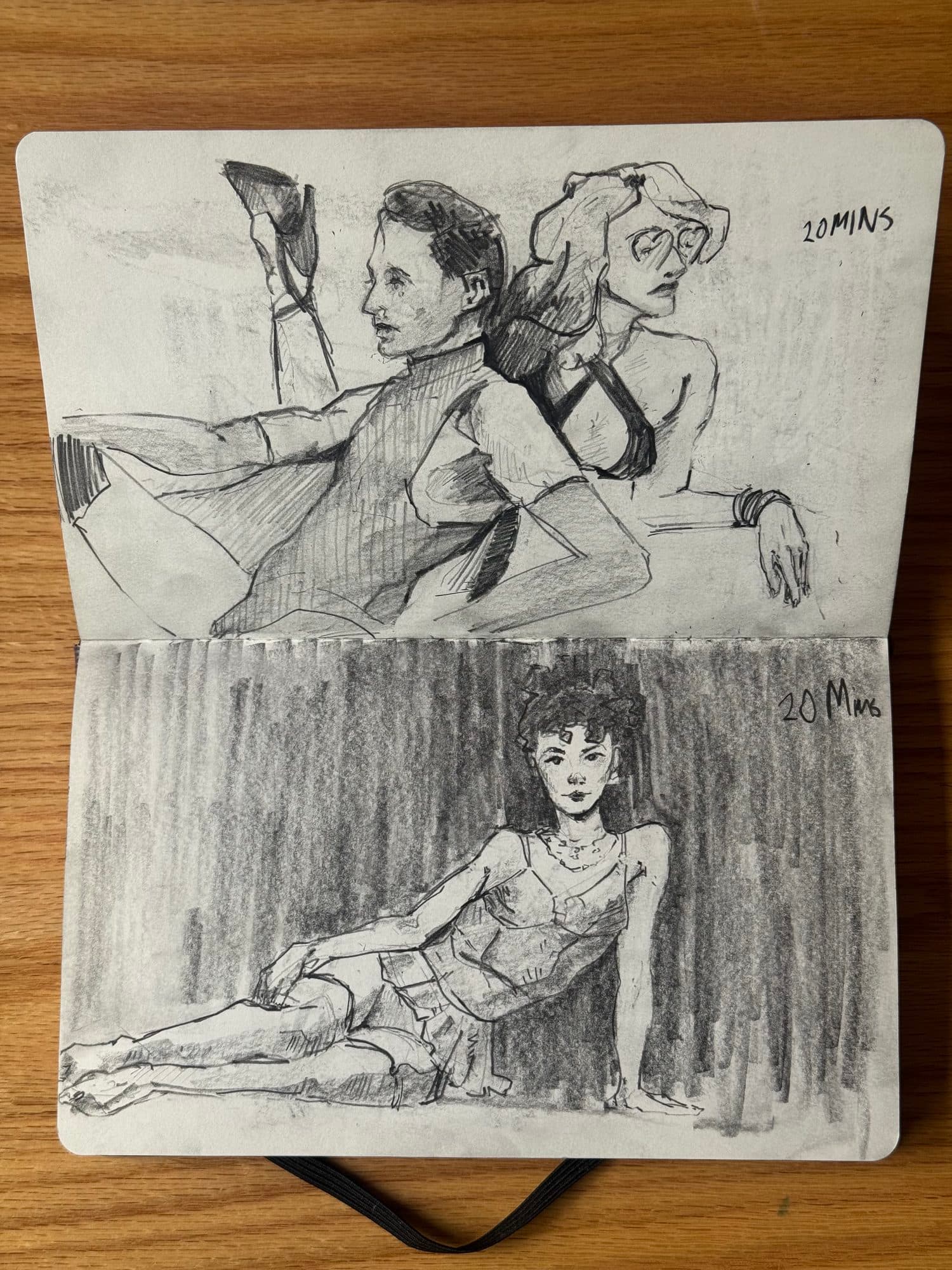 Sketchbook page of two twenty-minute graphite figure drawings: a reclining pair posed back to back and a short-haired woman lounging against a dark backdrop.